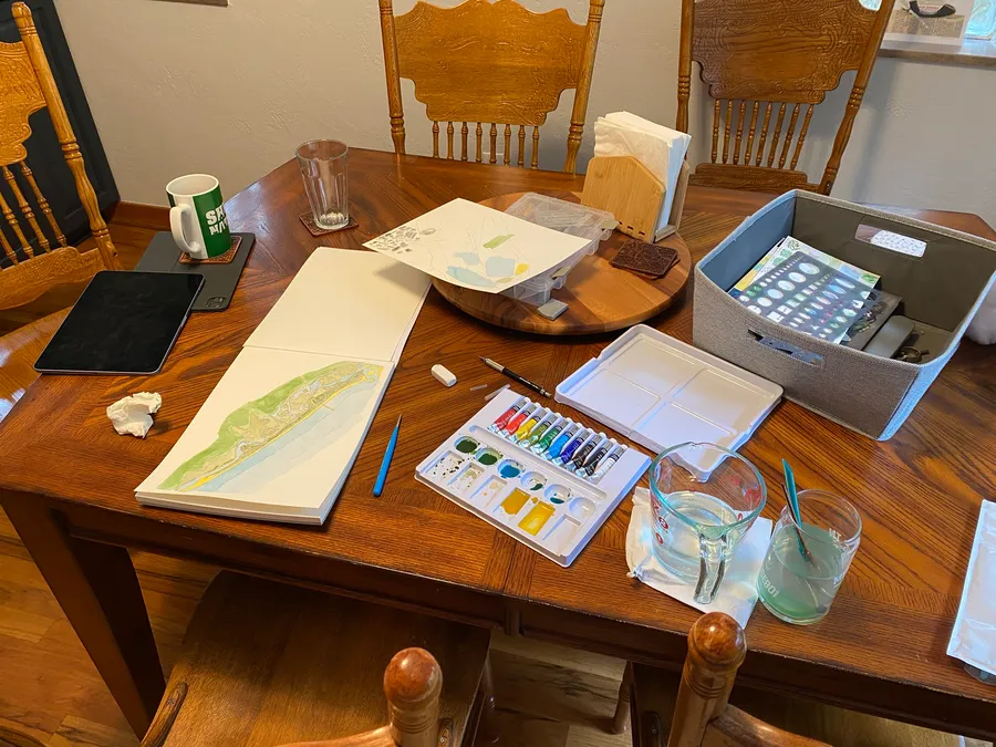 Watercolor map artwork and tools arranged on a work surface
